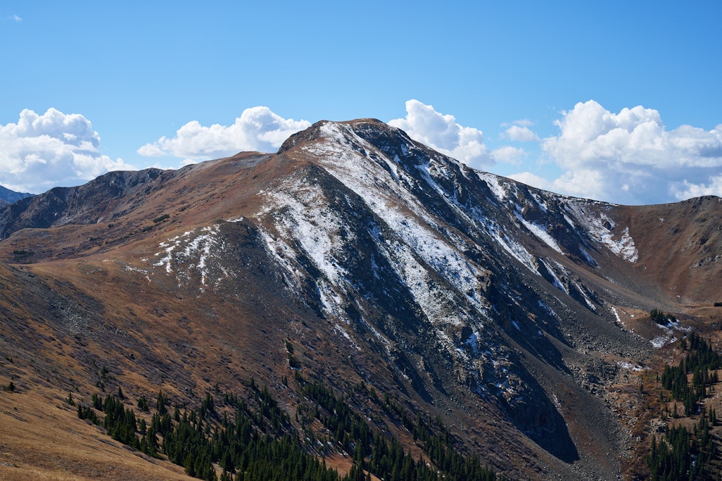 a wider shot of a mountain peak with snow and clouds, midday autumn sun