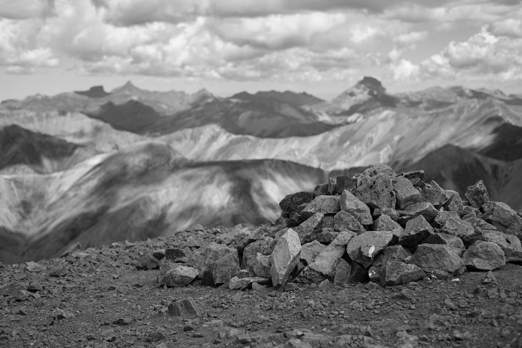 a pile of rocks forming a cairn on top of a mountain, looking out to other tall mountains