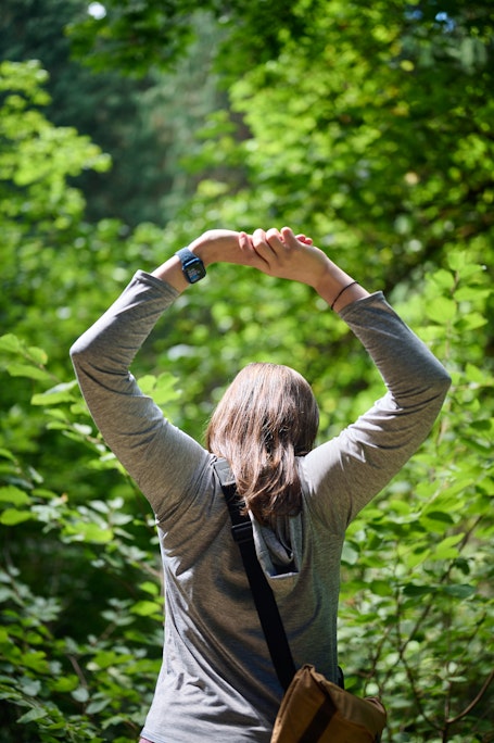 a person stretches their arms above their heads in a bright green forest