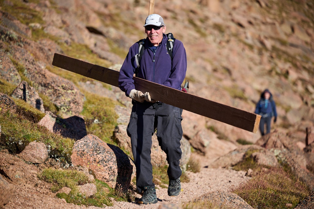 a smiling volunteer carrying a new support pole on Barr Trail
