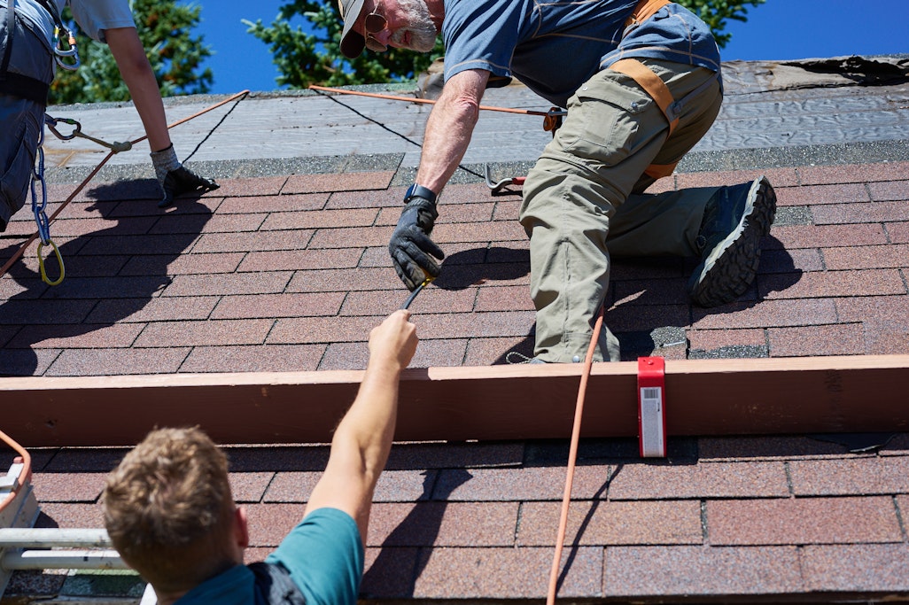 handing off a tool from someone on the ground to someone standing on the edge of the roof
