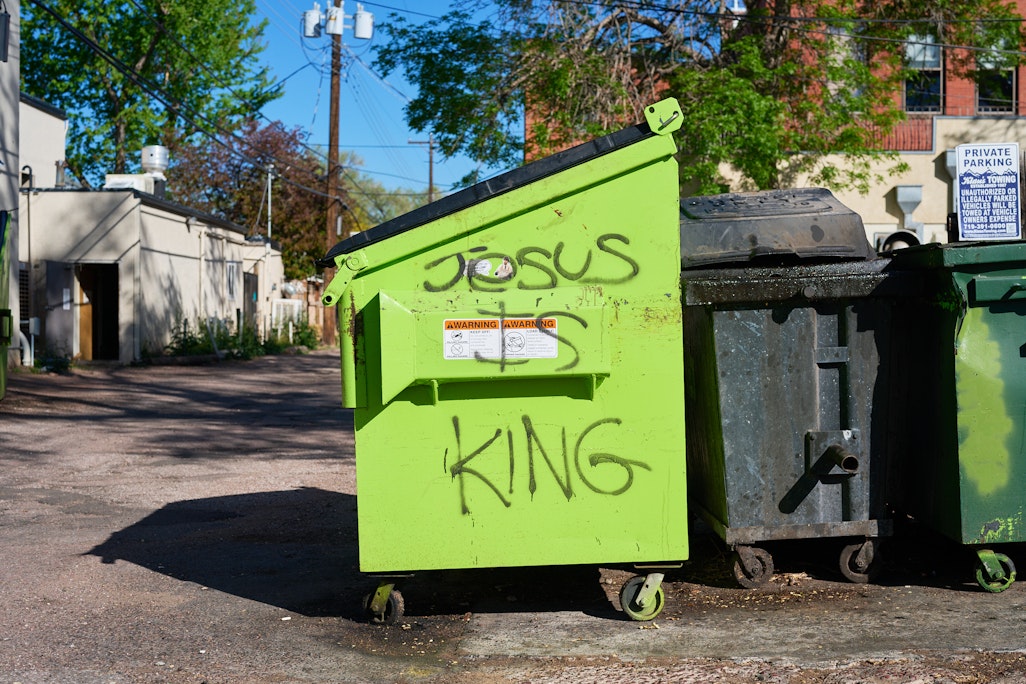 Jesus is King crudely written in black spray paint on a bright green dumpster in an alley