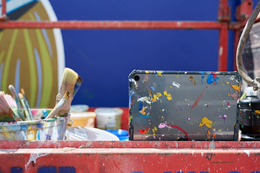 an iPad covered in paint, on a platform for a large-scale mural painting