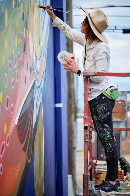 mural painter Molly McClure paints details on a boldly colored large-scale mural