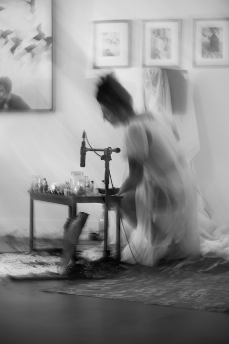 motion blurred movement of Jasmine Dillavou in a white translucent dress performing with hand-made instruments at a low table